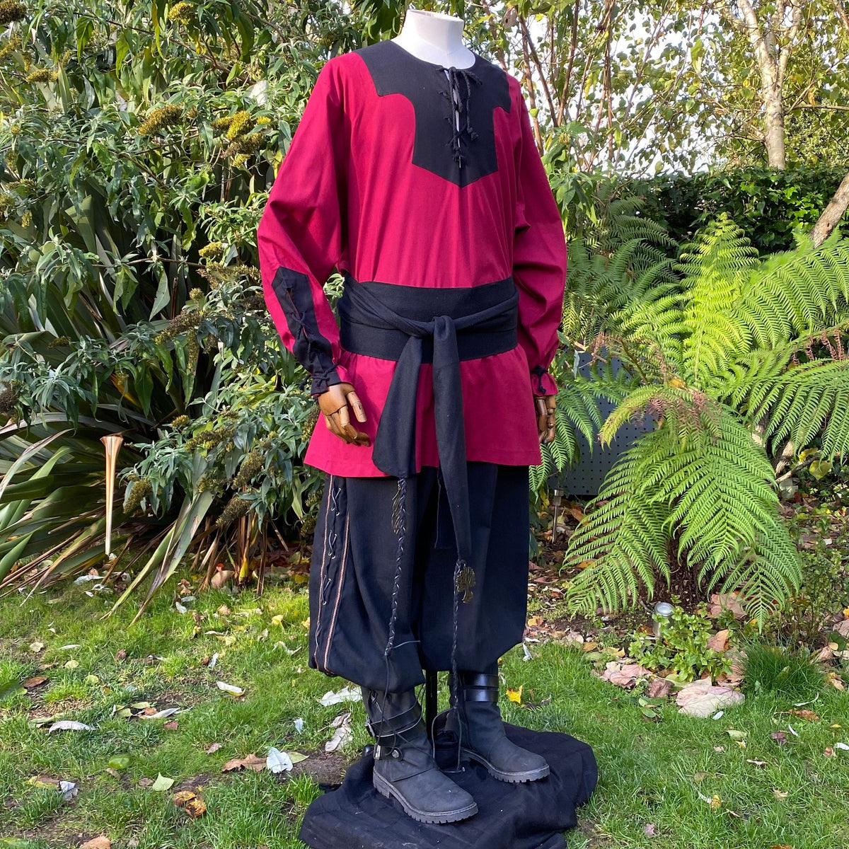 Medieval LARP attire with black boots and garden backdrop, side view.