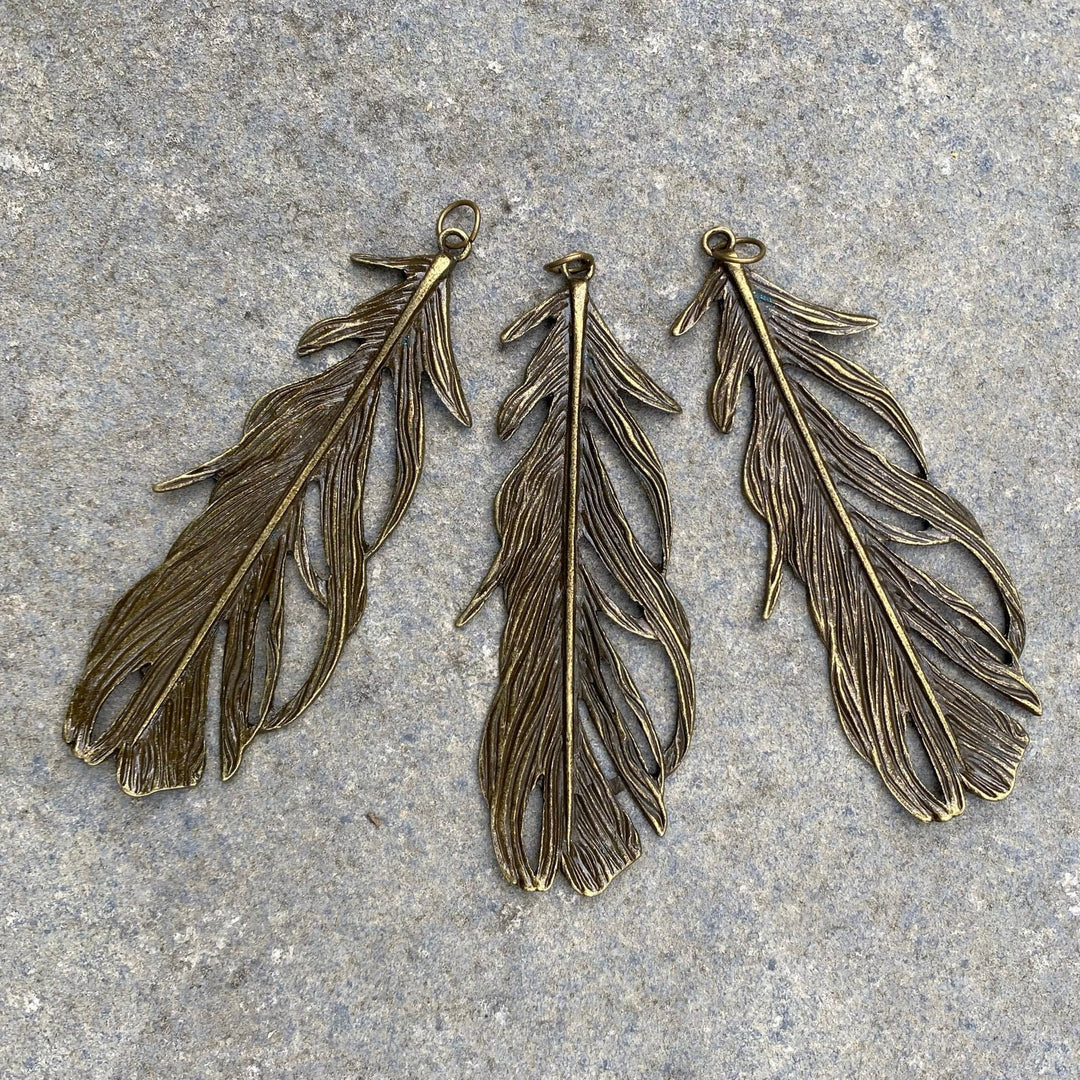 Three brass feather pendants on stone for LARP.