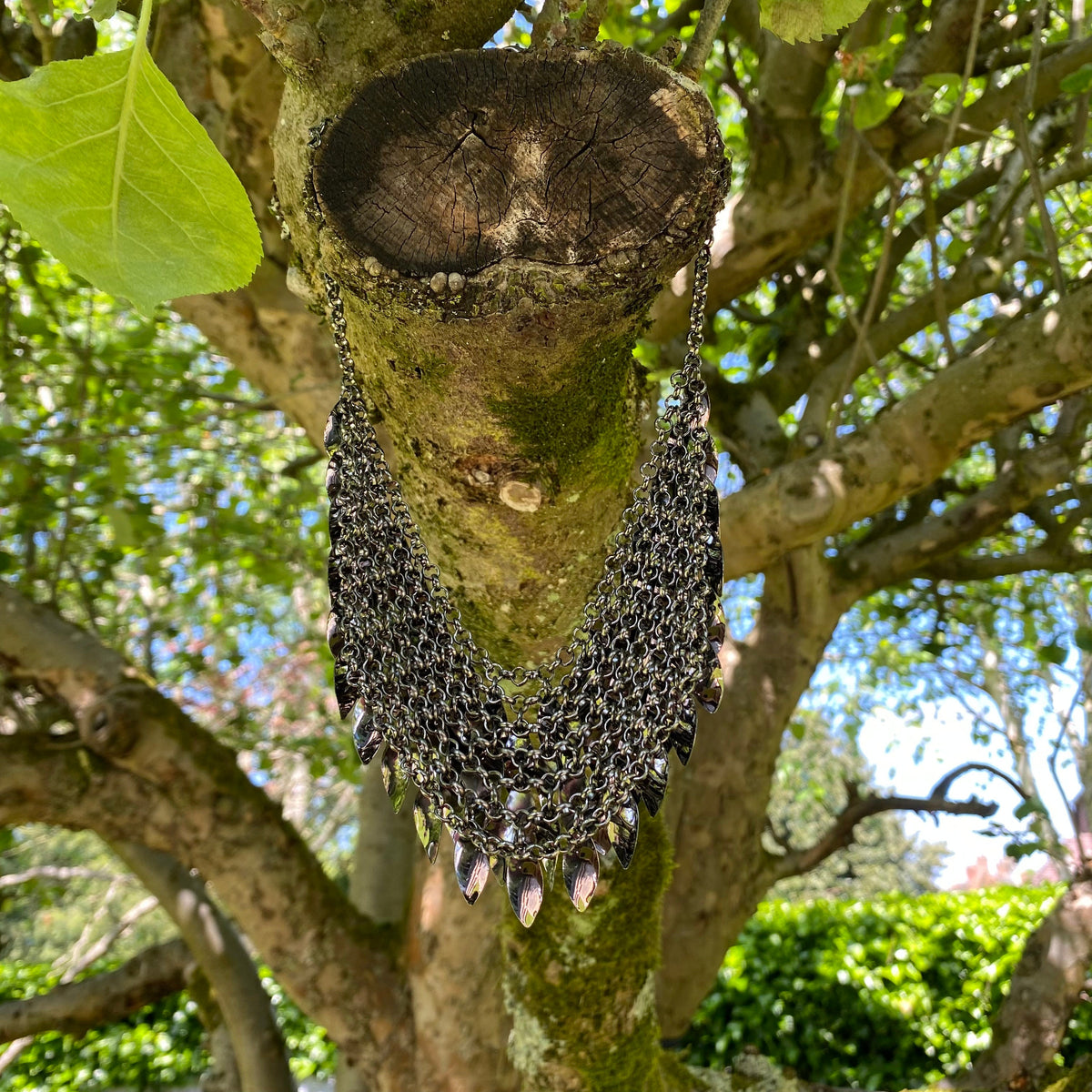 Dark silver chainmail necklace with layered leaves, draped on tree branch for LARP.