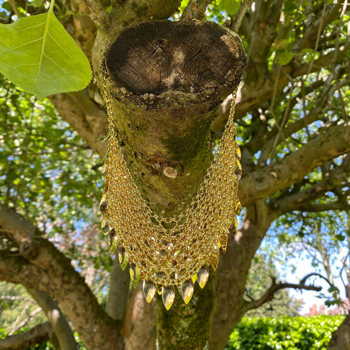 Gold layered chainmail necklace hanging on tree in medieval LARP setting.