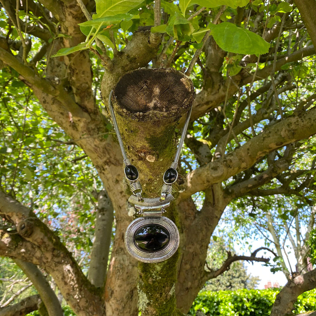 Silver Celtic LARP necklace with black gem hanging on a tree branch.