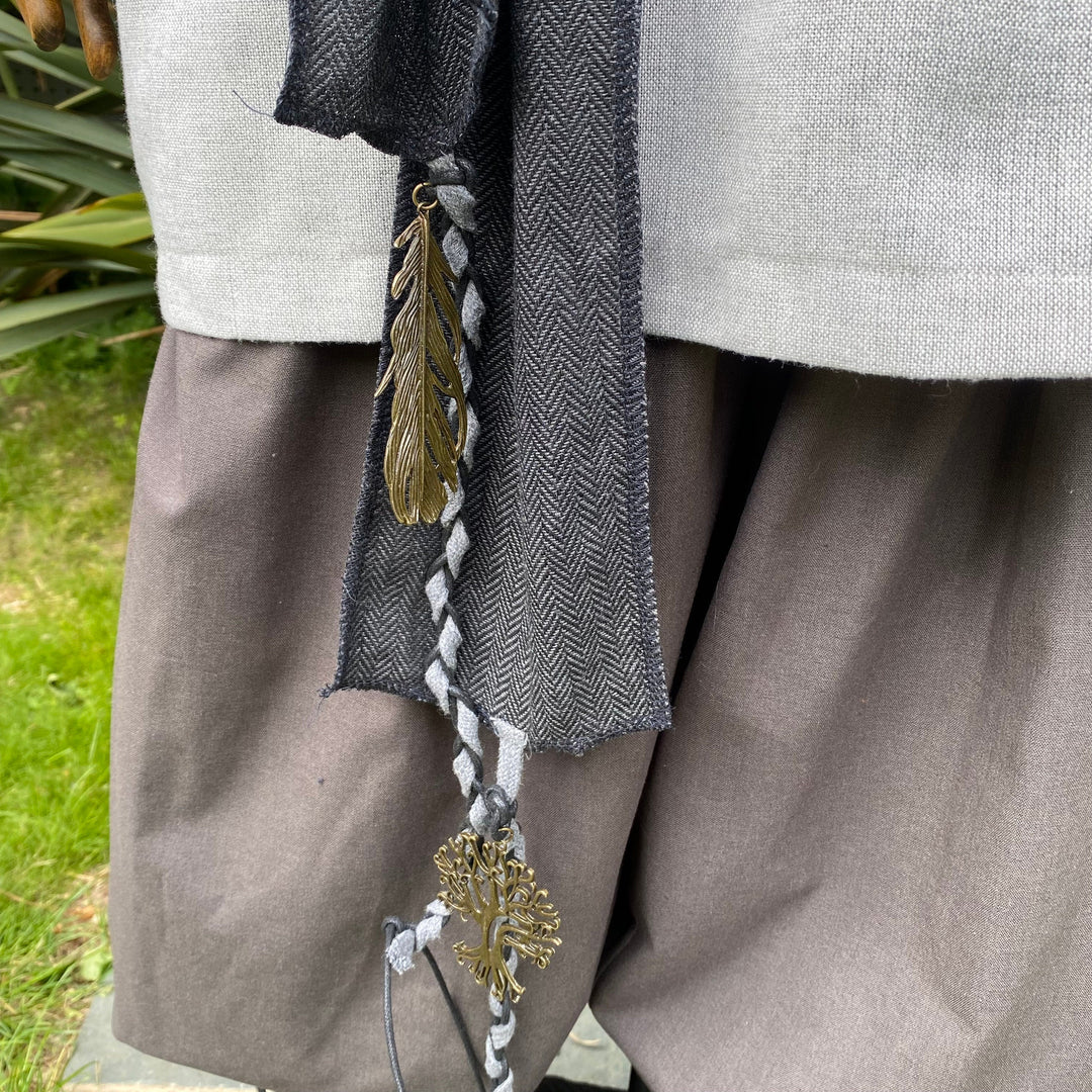 Medieval LARP sash close-up with feather and tree charms in wool fabric.