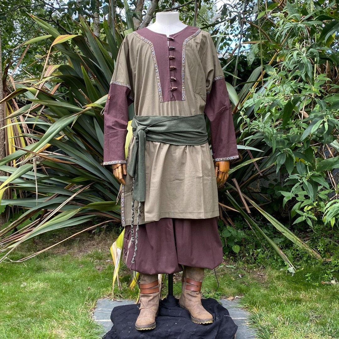 LARP tunic with green sash in garden setting, brown pants and detailed cuffs.