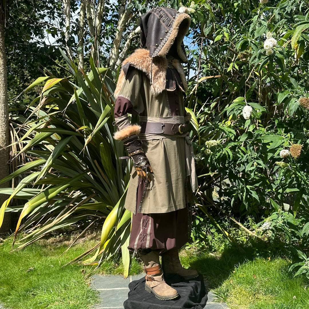 Profile view of medieval LARP ranger outfit, fur-trimmed hood, lush greenery.